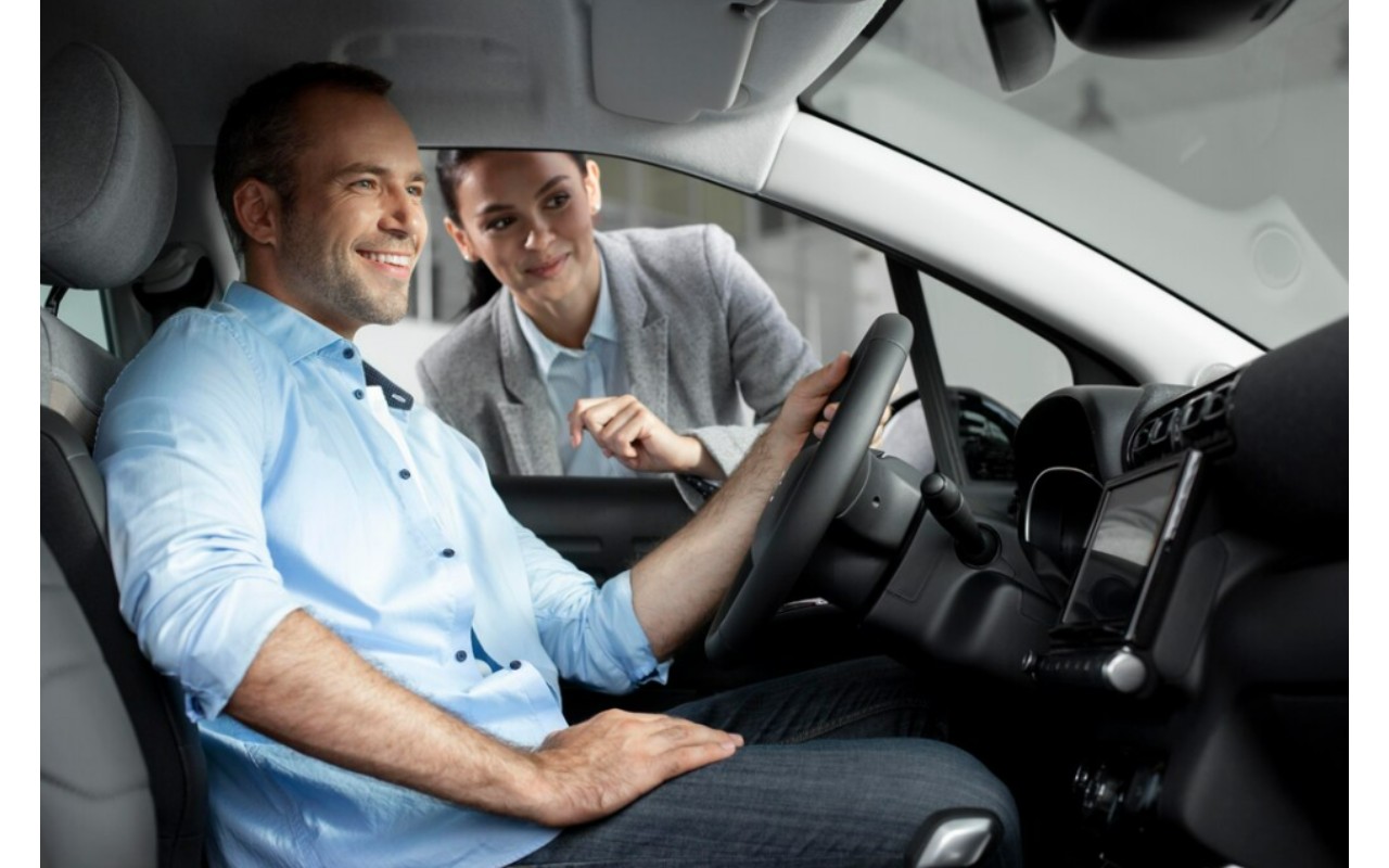 Asesora sonriente muestra el volante y controles a un cliente sentado en el asiento del conductor