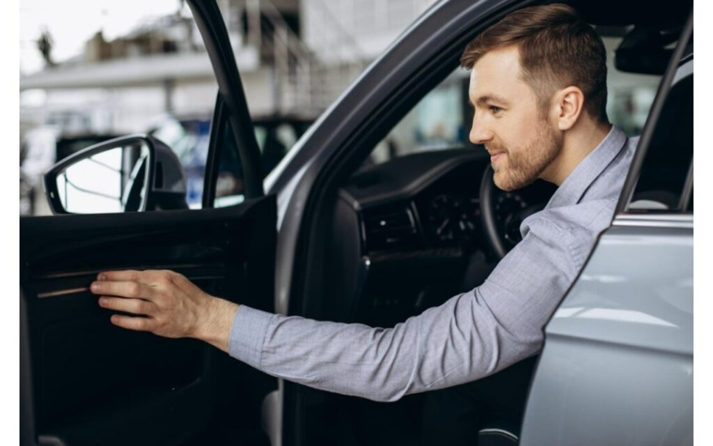 Hombre con saco gris sube a un auto gris con la puerta del conductor abierta