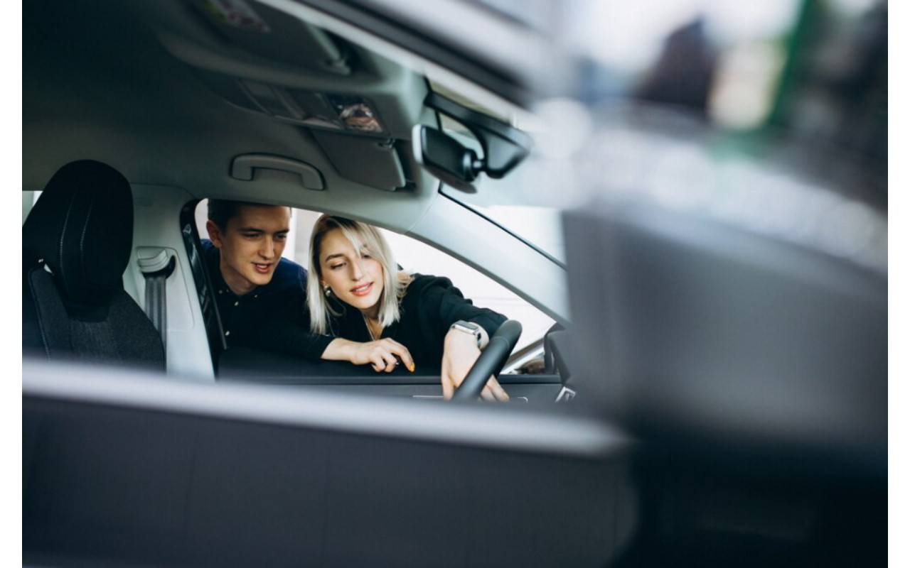 Hombre y mujer jóvenes inclinados sobre el asiento del conductor revisando los controles del vehículo