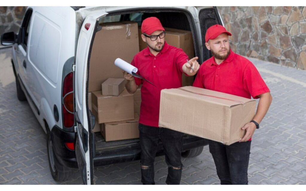 Dos repartidores de uniforme rojo cargan cajas frente a una furgoneta blanca de reparto